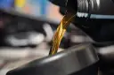 Goldfarbenes Motoröl fließt aus einem schwarzen Behälter in einen dunklen Trichter.