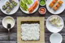 Przygotowanie sushi: ryż, nori, łosoś, awokado, wasabi i marynowany imbir na drewnianym blacie.
