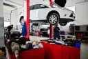 Warsztat samochodowy: biały samochód na podnośniku, mechanik w niebieskim kombinezonie.