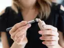 Dłonie z perfekcyjnym manicure nakładają pędzelkiem dr irena eris podkład rozświetlający na pociągłą tubkę.