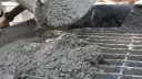 Świeży beton z kruszywem, idealny jako jaki beton pod obrzeża, wylewany z maszyny na ruszt.