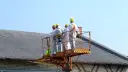 Pracownicy w kombinezonach na podnośniku przy dachu z eternitu. Zastanawiasz się, ile kosztuje usunięcie azbestu z dachu?