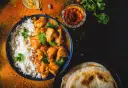 Pyszny Butter Chicken przepis: kremowy kurczak w sosie pomidorowym z ryżem i plackami naan, ozdobiony świeżą kolendrą i przyprawami.
