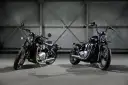 Dwa motocykle Triumph Bonneville Bobber w ciemnych kolorach, stojące obok siebie w industrialnym wnętrzu.