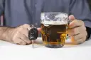 Dłoń trzymająca kufel piwa obok kluczyków samochodowych.