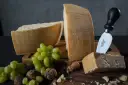 Kawałki parmezanu, winogrona i orzechy na drewnianych deskach. Widać wyraźne tłoczenia na skórce, które pokazują, jak wygląda parmezan.