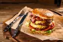 Podwójny burger z soczystym mięsem na burgery, serem, bekonem i warzywami, gotowy do zjedzenia z widelcem i nożem.