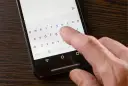 Dłoń naciska klawisz "Polski" na klawiaturze ekranowej smartfona.