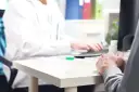 Pacjent czeka na decyzję o urlopie dla poratowania zdrowia. Lekarz pisze zalecenia na komputerze.