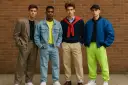 Czterech młodych mężczyzn prezentuje stylizacje w duchu moda męska lata 80.: garnitur, jeans, sweter z krawatem i bomberka z neonowymi spodniami.