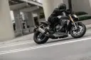 Motocyklista w kasku i skórzanej kurtce pochyla się na swoim motocyklu Triumph Speed Triple, pokonując zakręt na miejskiej drodze.