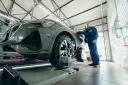 Mechanik w niebieskim kombinezonie stoi obok nowoczesnego samochodu na podnośniku w warsztacie.