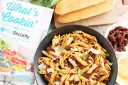 Makaron penne z suszonymi pomidorami, parmezanem i bazylią w czarnej misce, obok pieczywa i książki kucharskiej.