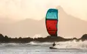 Kitesurfer na desce w akcji, z kolorowym latawcem na tle gór i morza.