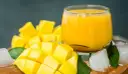 Orzeźwiający mango lassi przepis: pokrojony w kostkę dojrzały mango, szklanka gęstego napoju, kostki lodu i zielone liście.