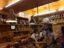 Interior of a bakery with shelves of bread, pastries, and bottles. Two women are behind the counter.