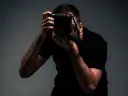 Mężczyzna w czarnej koszulce trzyma aparat fotograficzny i robi zdjęcie.