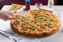 Pizza z krewetkami, oliwkami i kaparami na drewnianej desce, ręka podnosi kawałek.