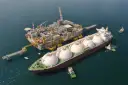 Praca na statku LNG: potężna jednostka z kopułami ładunkowymi przy platformie wydobywczej, holowniki asystują.