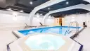 Wnętrze hotelowe z basenem, jacuzzi, sauną i leżakami.