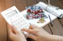 Ręce liczą na kalkulatorze przy modelu domu, monetach i dokumentach. Czy to podatek katastralny, co to?