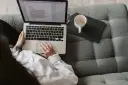 Kobieta pisze na laptopie, zastanawiając się, ile zarabia scenarzysta. Obok kubek i tablet.