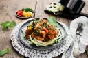 Spaghetti z cukinii z kurczakiem i warzywami w sosie na talerzu.