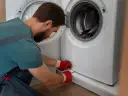 Mężczyzna w czerwonych rękawiczkach otwiera klapkę pralki, przygotowując się do jej czyszczenia. To pierwszy krok, jak odkamienić pralkę.