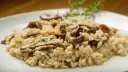 Kremowe risotto z grzybami na białym talerzu, ozdobione gałązką rozmarynu.