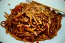 Makaron chow mein z sezamem i papryką na białym talerzu, z pałeczkami.