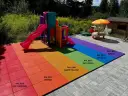 Kolorowy plac zabaw z tęczową nawierzchnią gumową i zjeżdżalnią.