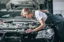 Młoda mechaniczka pochyla się nad silnikiem, sprawdzając go. To może być początek jej drogi, jak otworzyć warsztat samochodowy.