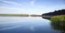 Spokojny zalew Dziećkowice z odbijającymi się w tafli wody chmurami i zielonym lasem w tle.