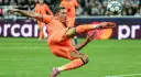 Piłkarz w pomarańczowym stroju wykonuje akrobatyczne kopnięcie do piłki. To Robert Lewandowski, który gra w Lidze Mistrzów.