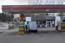 Station TotalEnergies avec une camionnette blanche en cours de ravitaillement. Panneaux de prix et de services.