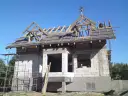 Budowa domu w toku. Na szczycie dachu, wśród drewnianej konstrukcji, widoczna jest ozdobna wiecha.