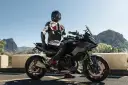 Motocyklista w kombinezonie na czarnym motocyklu BMW, gotowy do podróży po górskich drogach. Wśród wielu marek motocykli, ta prezentuje się imponująco.