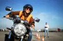 Uśmiechnięta kursantka w kamizelce odblaskowej i kasku na motocyklu, przygotowuje się do egzaminu na prawo jazdy A2.