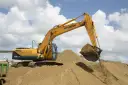 Koparka Hyundai z łyżką pełną piasku nad zwałami. Zastanawiasz się, ile kosztuje tona piasku?