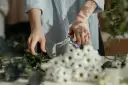 Dzień florysty. Dłonie przycinają zielone gałązki, obok bukiet białych kwiatów.