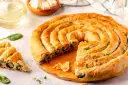 Złocisty borek ze szpinakiem, zwinięty w spiralę, kusi chrupiącym ciastem i aromatycznym nadzieniem. Obok kilka porcji i świeże liście szpinaku.