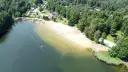 Słoneczny dzień nad jeziorem Rogoźnik. Ludzie kąpią się i opalają na piaszczystej plaży, otoczonej zielonym lasem.
