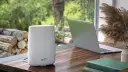 Ein weißer Orbi WLAN-Router steht neben einem Laptop auf einem Holztisch.