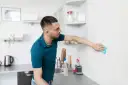 Mężczyzna wyciera niebieską ściereczką białą ścianę w kuchni.