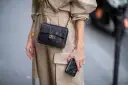 Elegancka kobieta w beżowym płaszczu prezentuje klasyczną, pikowaną torebkę Chanel vintage z złotym łańcuszkiem i logo.