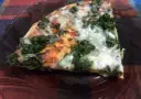 Kawałek pysznej pizzy ze szpinakiem, z ciągnącym się serem i pomidorowym sosem, na ciemnym talerzu.