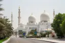 Wielki Meczet Szejka Zajida w Abu Zabi z minaretami i kopułami, otoczony palmami.