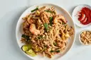 Pyszny Pad Thai przepis: makaron ryżowy z krewetkami, jajkiem, orzeszkami ziemnymi i szczypiorkiem. Obok chili i orzeszki.