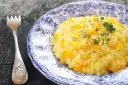 Kremowe risotto z dynią na talerzu z niebieskimi wzorami, obok widelca.