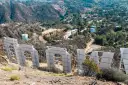 Widok zza gigantycznych liter znaku Hollywood. W oddali widać wzgórza z domami i drogami.